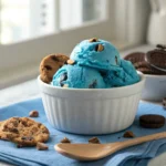 Close-up of blue Cookie Monster ice cream with chocolate chip cookies and Oreos in a white bowl.