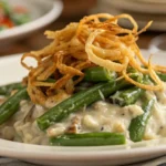 Close-up of green bean casserole on a white plate with creamy beans and crispy onions.