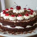 A multi-layered Black Forest cake with chocolate layers, whipped cream, cherry filling, and topped with cherries and chocolate shavings.