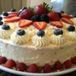 A Chantilly cake topped with whipped cream frosting, fresh strawberries, blueberries, blackberries, and raspberries, served on a white plate.
